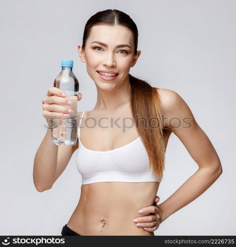 young sporty woman over gray background drinking water. sporty woman over gray background drinking water