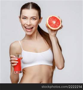 young sporty woman over gray background holding glass of orange juice. sporty woman over gray background holding glass of grapefruit juice