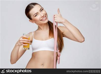 young sporty woman over gray background holding glass of orange juice. sporty woman over gray background holding glass of orange juice