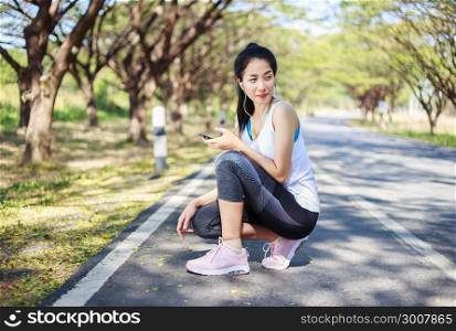 young sporty woman sitting on the road in the park and using smartphone with earphone to listening music