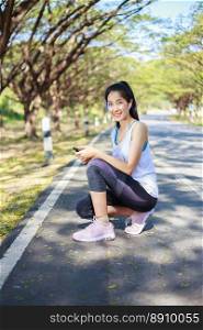 young sporty woman sitting on the road in the park and using smartphone with earphone to listening music