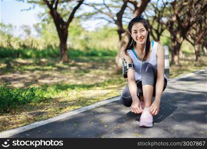 young sporty woman tying shoelaces while listening to music with earphones from her smartphone in the park