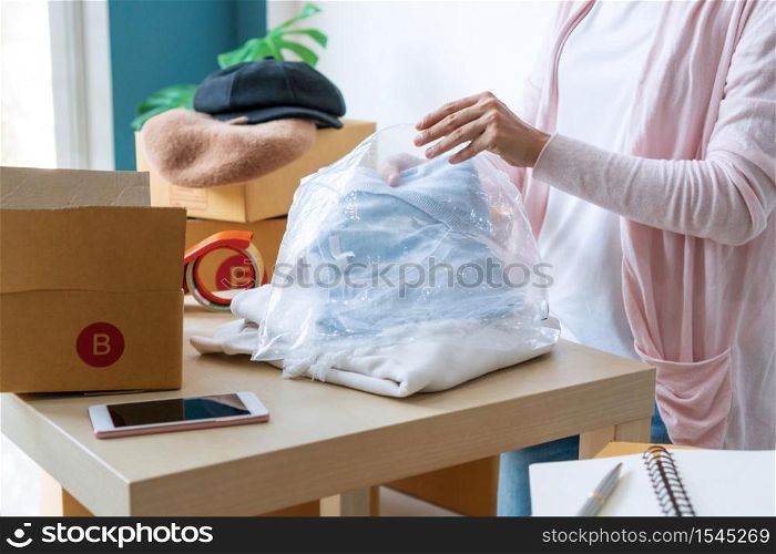 Young start up business owner packing cardigan on the table at workplace. Freelance woman seller prepare product for packaging process. Online selling, packing concept. Close up
