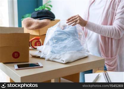 Young start up business owner packing cardigan on the table at workplace. Freelance woman seller prepare product for packaging process. Online selling, packing concept. Close up