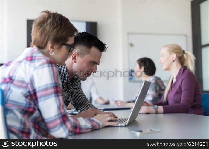 young startup business people, couple working on laptop computer, businesspeople group on meeting in background at office interior