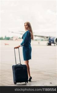 Young stewardess with suitcase on aircraft parking, tail of the airplane on background. Air hostess in suit with luggage, flight attendant occupation, aviatransportations job. Young stewardess with suitcase on aircraft parking