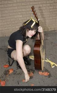 Young street performer pelted with tomatos and bananas sits broken hearted with her guitar.