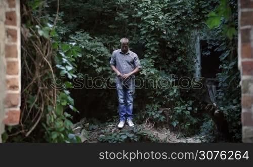 Young street style dancer dressed in urban style dancing in abandoned building. Man dancing street dance over green trees and plants background