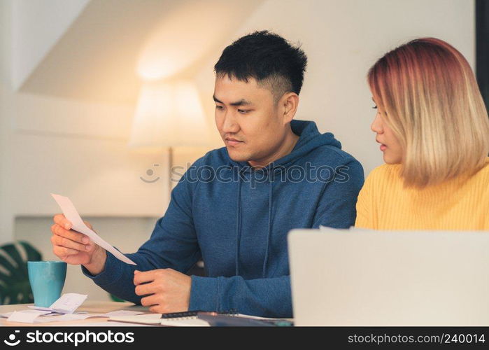 Young stressed asian couple managing finances, reviewing their bank accounts using laptop computer and calculator at modern home. Woman and man doing paperwork together, paying taxes online.