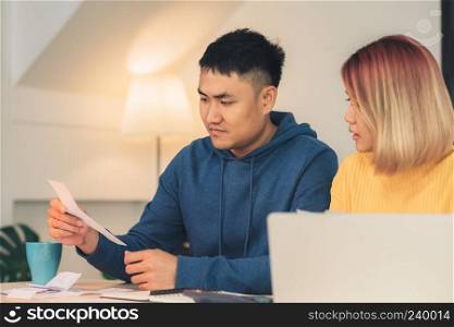 Young stressed asian couple managing finances, reviewing their bank accounts using laptop computer and calculator at modern home. Woman and man doing paperwork together, paying taxes online.