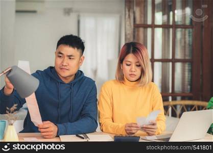 Young stressed asian couple managing finances, reviewing their bank accounts using laptop computer and calculator at modern home. Woman and man doing paperwork together, paying taxes online.
