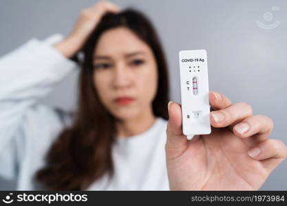 young stressed woman holding Coronavirus(Covid-19) positive test result with Antigen Rapid Test kit (ATK)