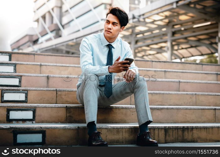 Young Striving Asian Businessman Sitting on Staircase in the City. hand holding a Mobile Phone