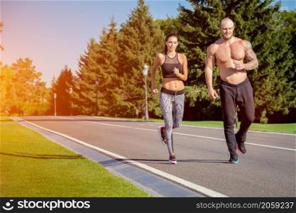 Young strong male and female fitness models outdoors in beautiful landscape. Man and woman running in park at sunset. Man and woman running in park