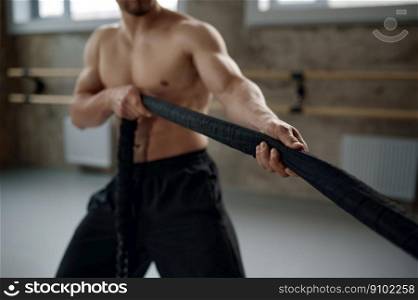 Young strong man pulling training sports rope front view. Male athlete doing workout exercises at gym. Closeup view. Young strong man pulling training sports rope front view
