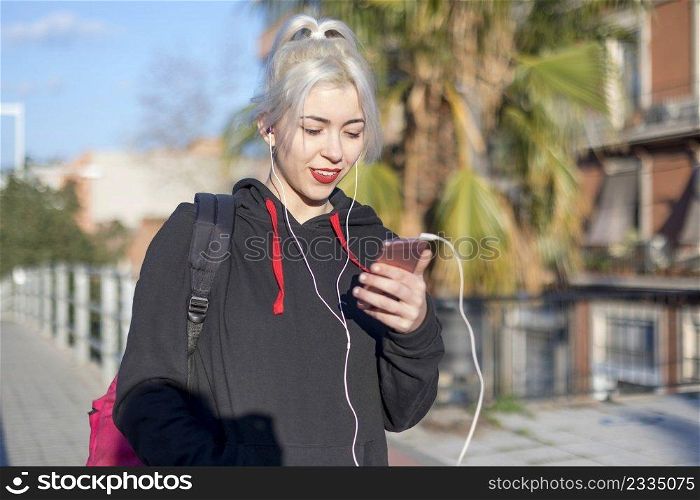 Young student blonde woman sitting on railing while using a mobile