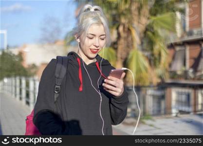 Young student blonde woman sitting on railing while using a mobile