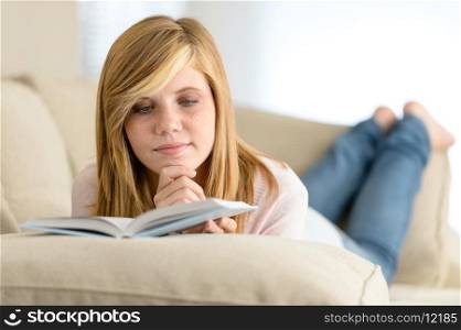Young student girl reading book lying on sofa
