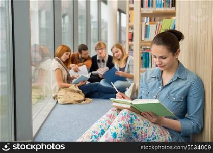 Young student sitting in college library with friends in background