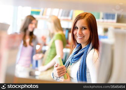 Young student woman choosing book among library shelves