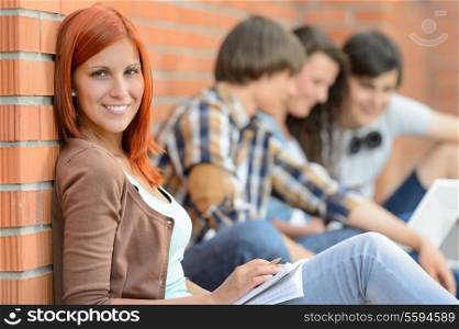 Young student woman sitting outside college friends in background