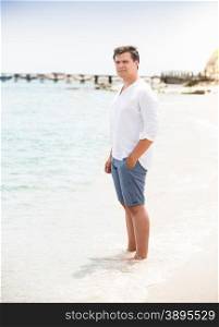 Young stylish man in shirt and shorts standing on the beach