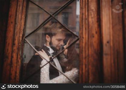 Young stylish newlyweds are hugging behind old rustic wooden door. wedding day. Young stylish newlyweds are hugging behind old rustic wooden door. wedding day.