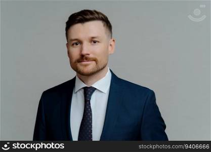 Young successful bearded businessman in suit, confident CEO, headshot posing, grey studio background.