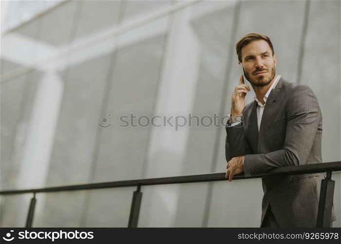 Young successful busi≠ssman wearing grey suit and holding his smartpho≠whi≤standing≠ar modern office or skyscrapers