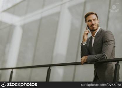 Young successful busi≠ssman wearing grey suit and holding his smartpho≠whi≤standing≠ar modern office or skyscrapers