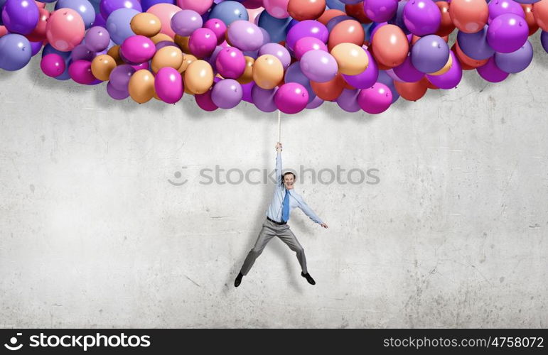 Young successful businessman flies on bunch of colorful balloons. Man flying in sky