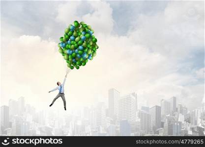 Young successful businessman flies on bunch of colorful balloons. Man flying in sky