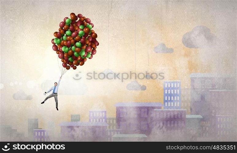 Young successful businessman flies on bunch of colorful balloons. Man flying in sky