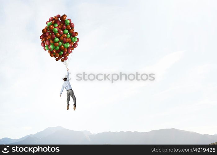 Young successful businessman flies on bunch of colorful balloons. Man flying in sky