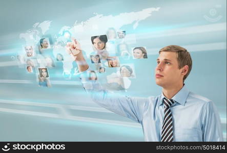 Young successful man looking at worldmap with profile photos of his colleagues and touching virtual screen. International communication concept.