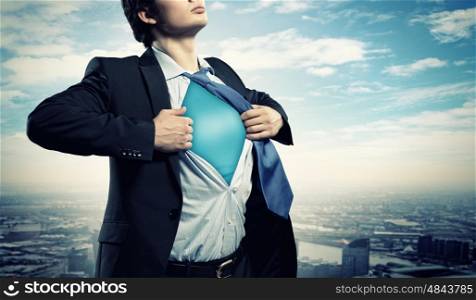 Young superhero businessman. Image of young businessman showing superhero suit underneath his shirt standing against city background