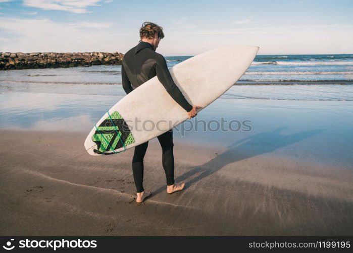 Young surfer entering into the water with his surfboard in a black surfing suit. Sport and water sport concept.