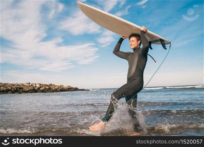 Young surfer entering into the water with his surfboard in a black surfing suit. Sport and water sport concept.