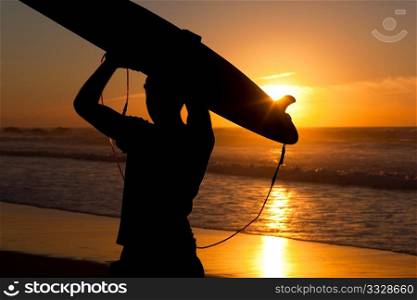 Young surfer on the beach with his surf board over the head, looking at the ocean