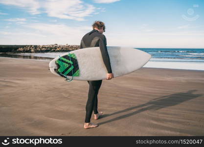 Young surfer standing in the ocean with his surfboard in a black surfing suit. Sport and water sport concept.