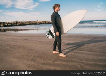 Young surfer standing in the ocean with his surfboard in a black surfing suit. Sport and water sport concept.