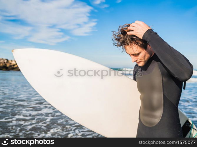 Young surfer standing in the ocean with his surfboard in a black surfing suit. Sport and water sport concept.