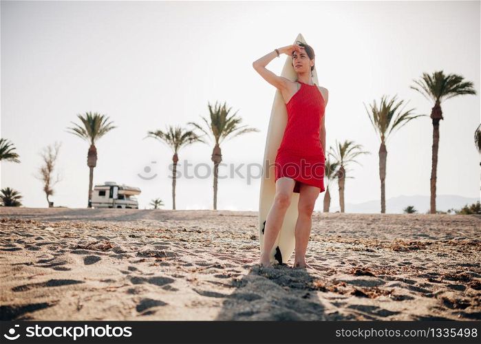 Young surfer woman covering face by hand from sun with surfboard