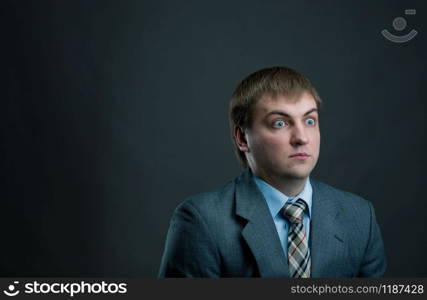 Young surprised businessman in suit and tie on black background. Thoughtful businessperson, male manager shocked. Young pensive businessman on black background