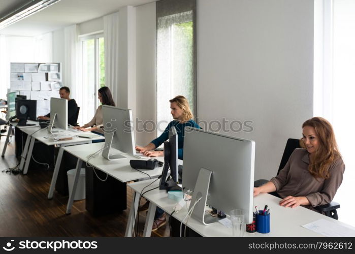 Young team working on computers at desks in stylish office with conceptual papers in the background, might be a startup or a creative office