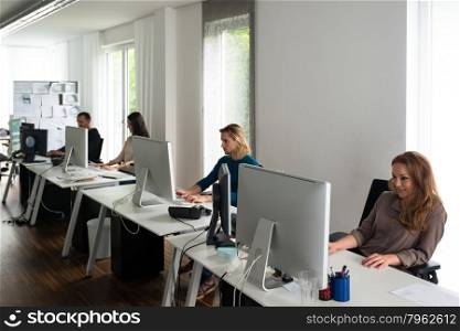Young team working on computers at desks in stylish office with conceptual papers in the background, might be a startup or a creative office