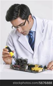 Young technician repairing machine part at table over gray background