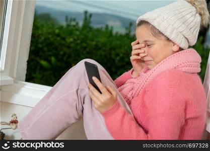 young teen girl with a pink sweater and a winter cap using a phone