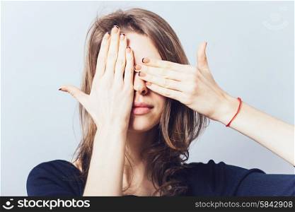 Young teen woman covering her eyes isolated on a gray background