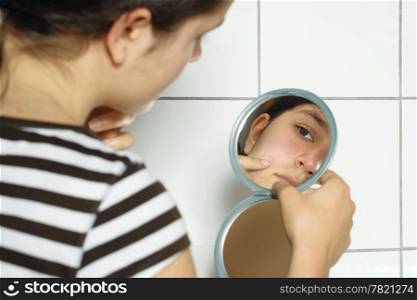Young teenage female holding a mirror looking at her complexion with concern.
